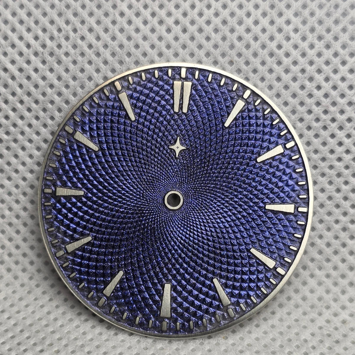 Blue textured watch dial with exposed metal baton markers and a star at twelve